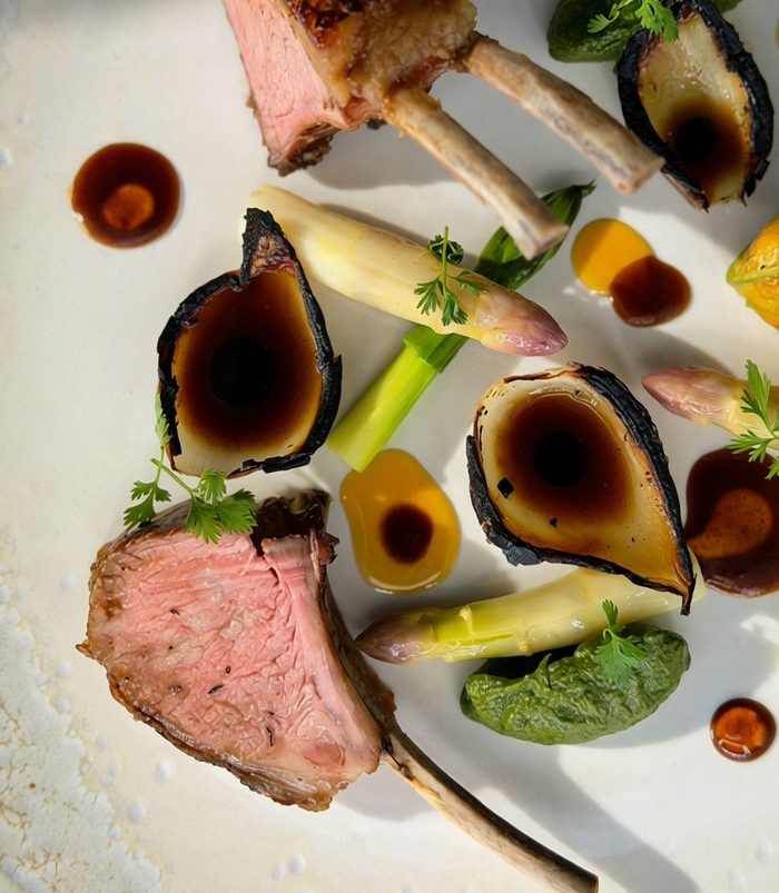 Carré d'agneau rôti, asperges grillées, oignon brûlé, condiment aux herbes et jus d'agneau — assiette de Romain Perrollaz